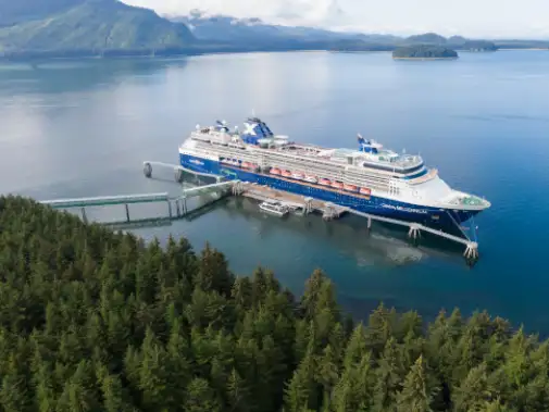 A large Celebrity Cruise ship docked at icy Strait Point surrounded by lush green forests and mountains