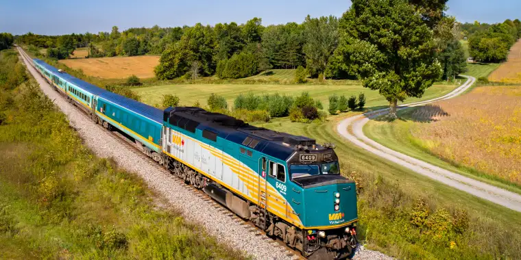 A VIA Rail train traversing scenic fields in Eastern Canada