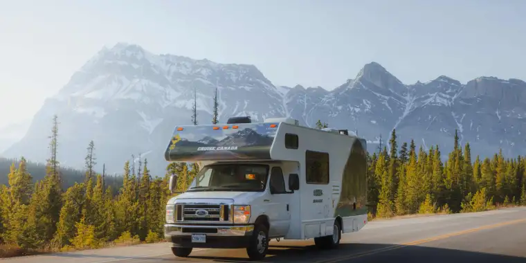 A Cruise Canada RV travelling on a scenic road in Canada with snow-capped mountain peaks on the background