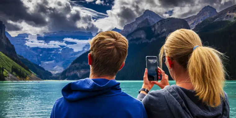 A woman takes a picture of a scenic turquoise lake in the Canadian Rockies