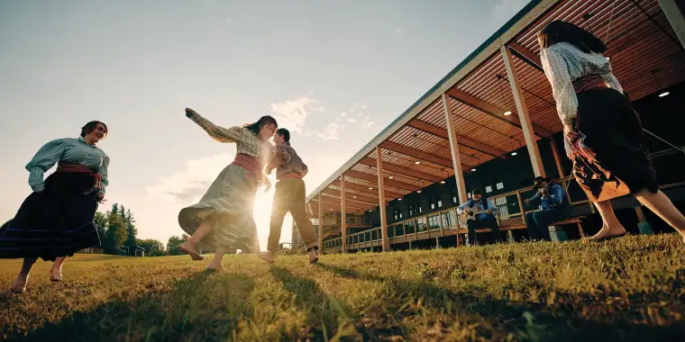 People dance in traditional dress in front of the setting sun