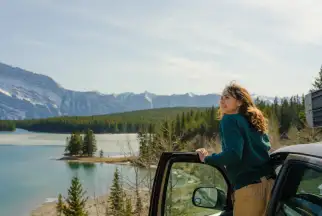 Woman leans out of a parked car looking at a scenic Canada mountain landscape