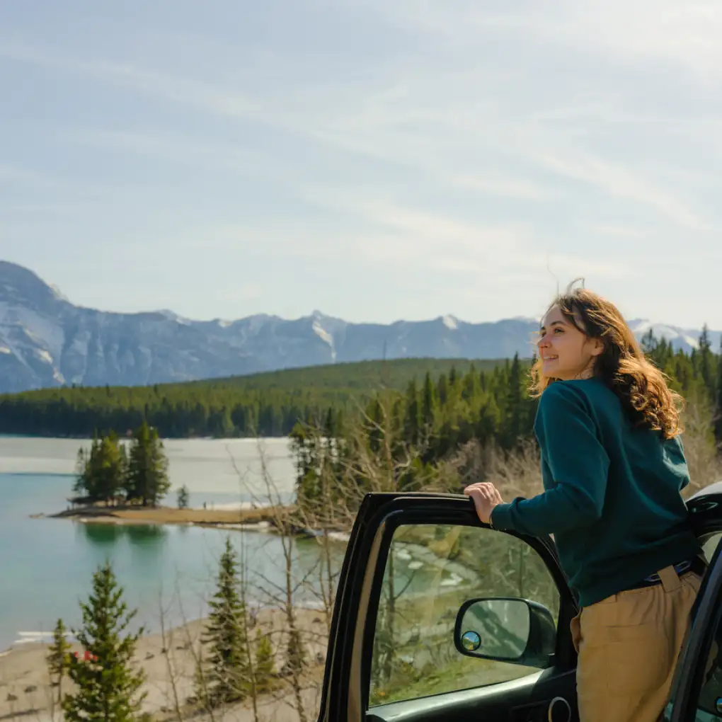 Woman leans out of a parked car looking at a scenic Canada mountain landscape