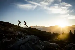 A couple hike up a picturesque mountain slope in Whistler as the sun rises behind them
